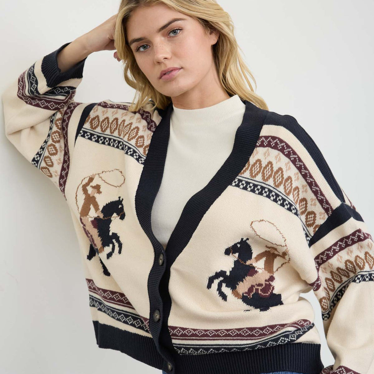 Woman modeling a three-button cardigan with horse motif and long sleeves.